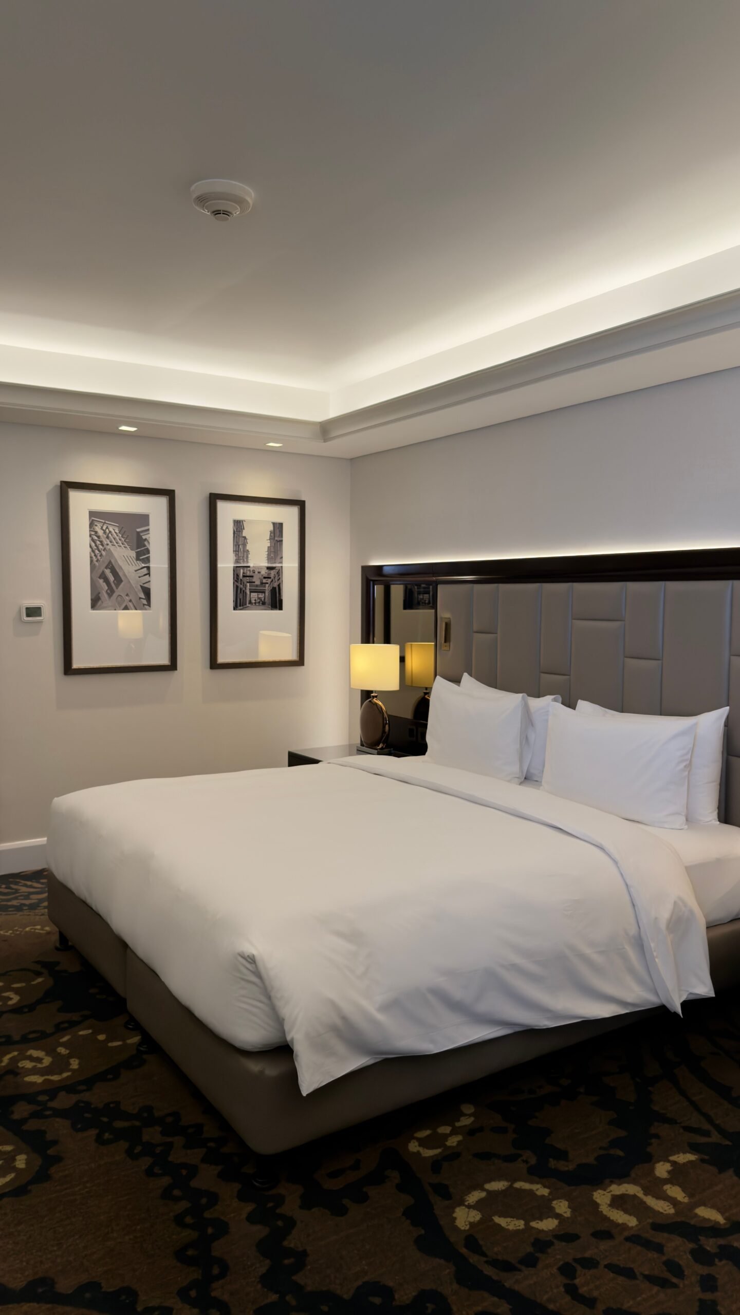 Modern hotel room with luxurious bedding and stylish decor, featuring framed cityscape art.